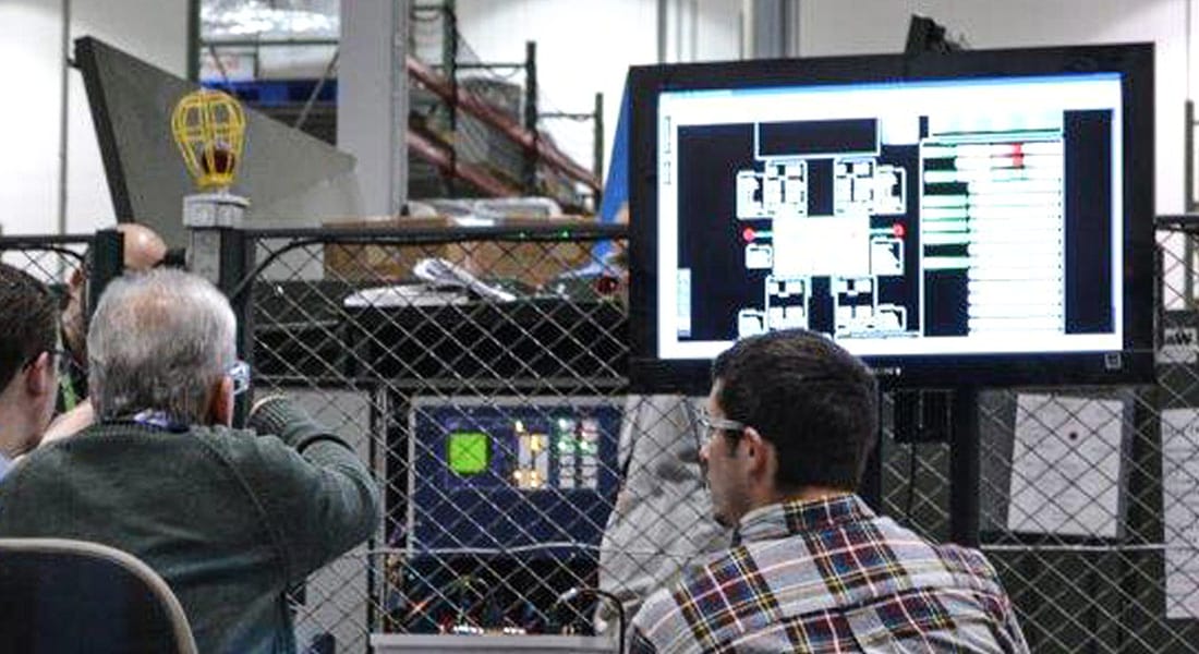Two men sitting in a factory looking at a TV screen